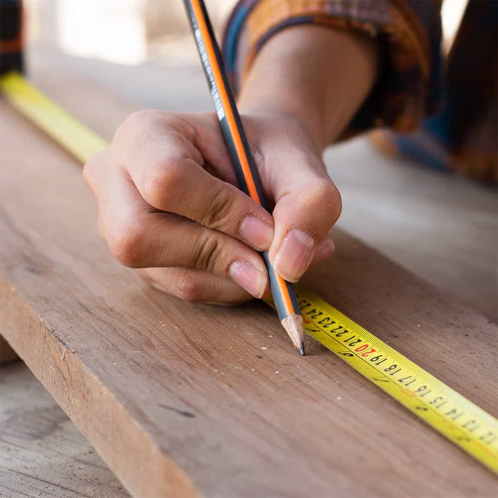 Hand measuring and marking wood with a pencil and tape measure, illustrating precision in construction and roofing projects.