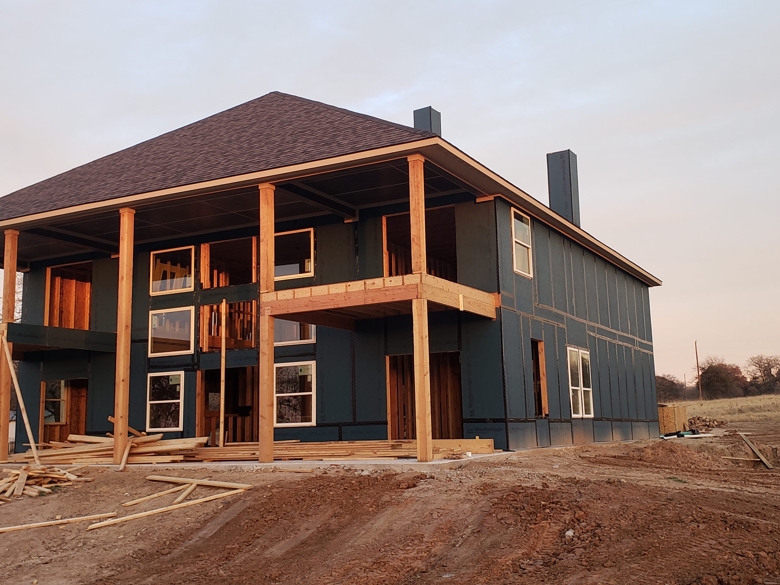 Two-story residential building under construction with exposed framing, sheathing, and wooden supports, showcasing energy-efficient design elements in a sunset setting.