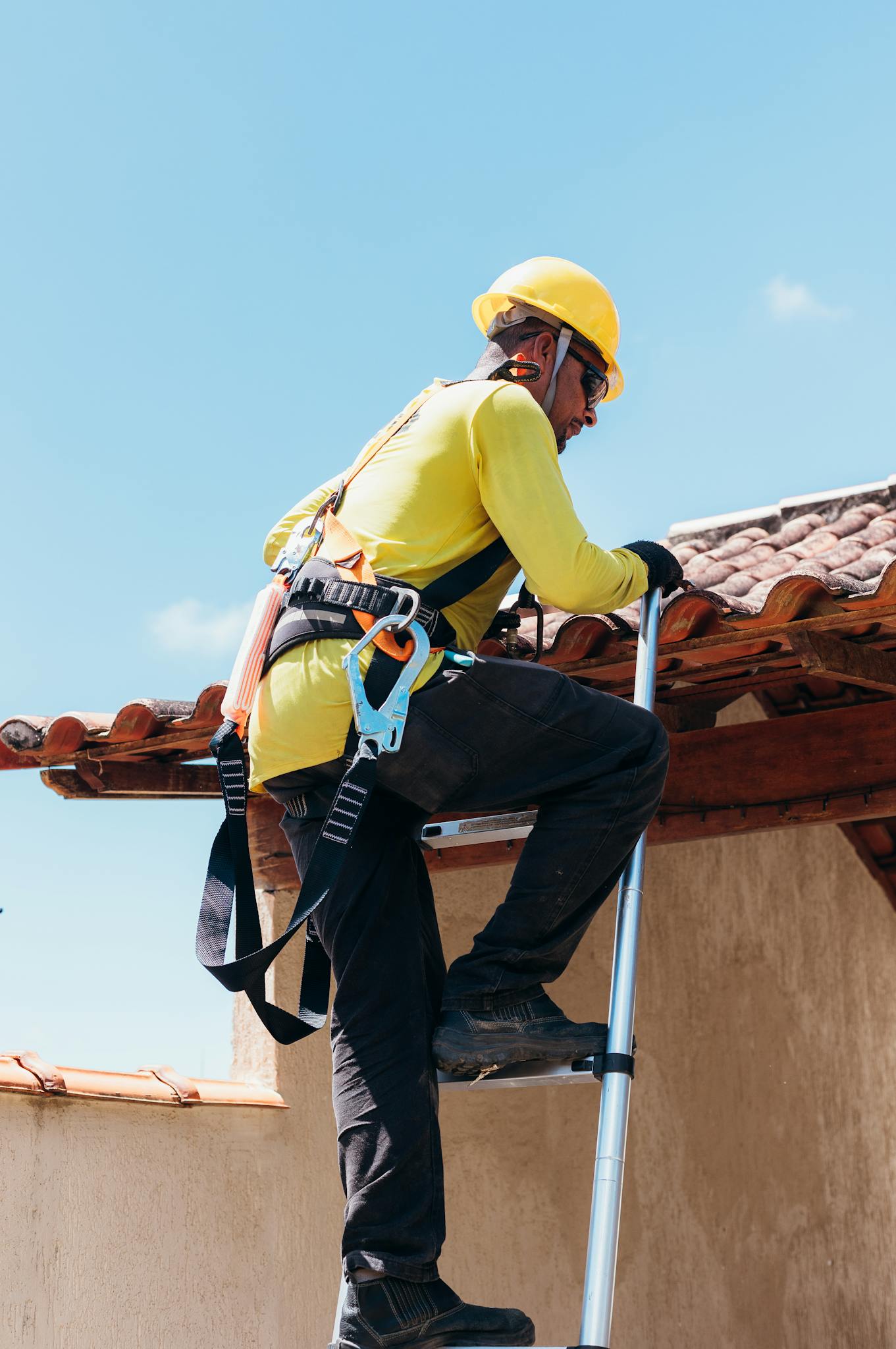 Professional construction worker safely ascending a ladder, wearing a hard hat and harness, on a roofing project in Fort Worth, Texas.
